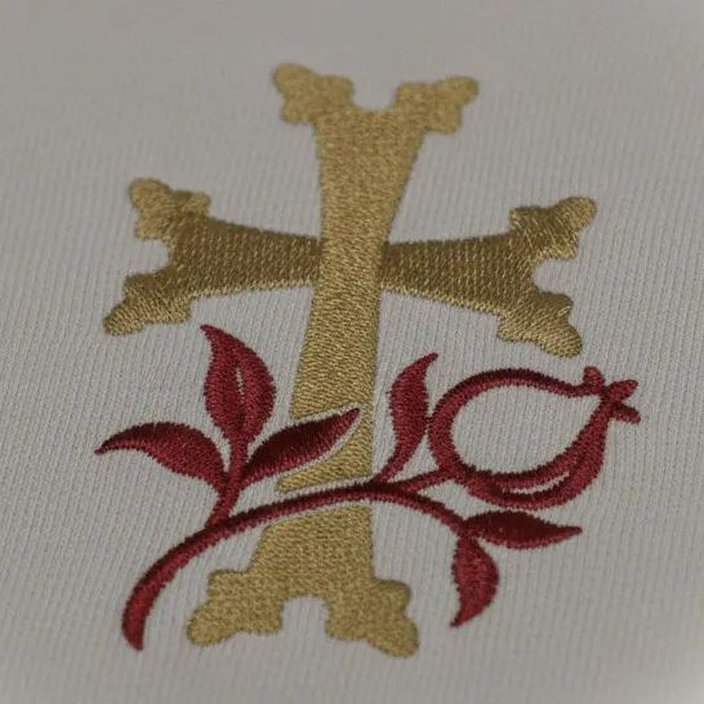 a close-up view of a gold cross with red leaves and branches, creating a striking contrast against the white background.